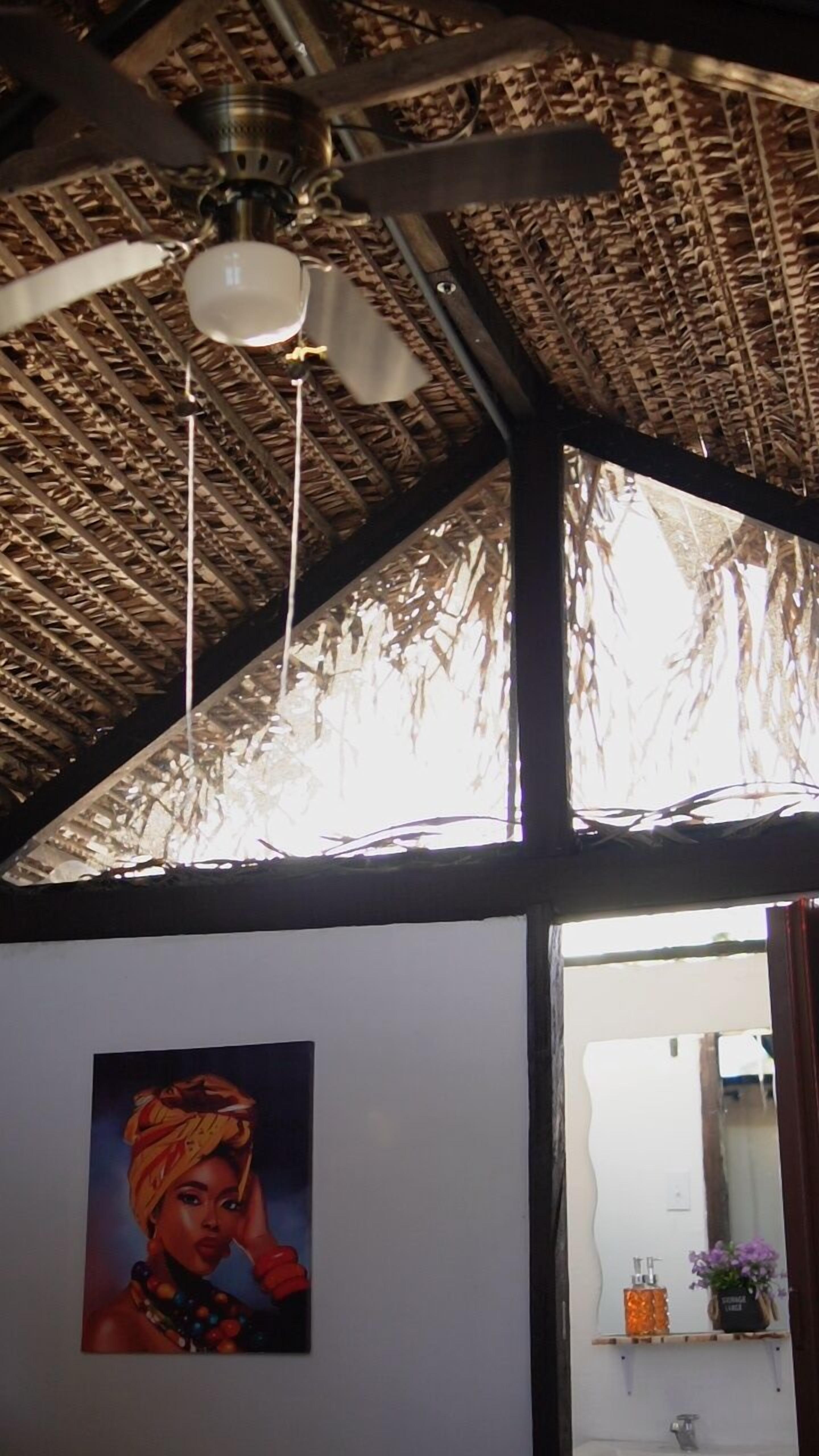 Una habitación con techo de paja, ventilador de techo y un cuadro en la pared.