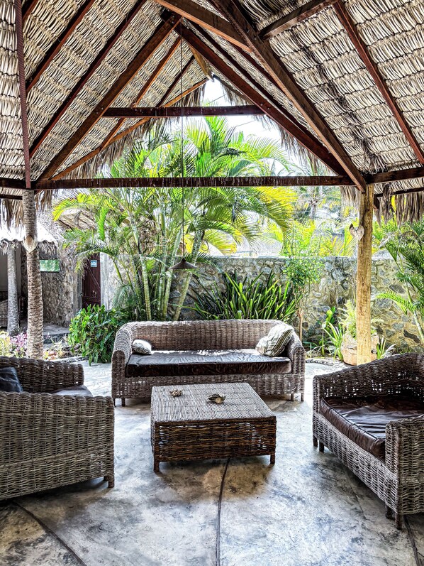 A covered outdoor seating area with wicker furniture and a thatched roof.