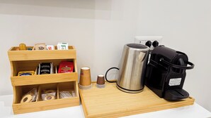 Una estación de café de madera con cafetera, hervidor y diferentes cápsulas de café.