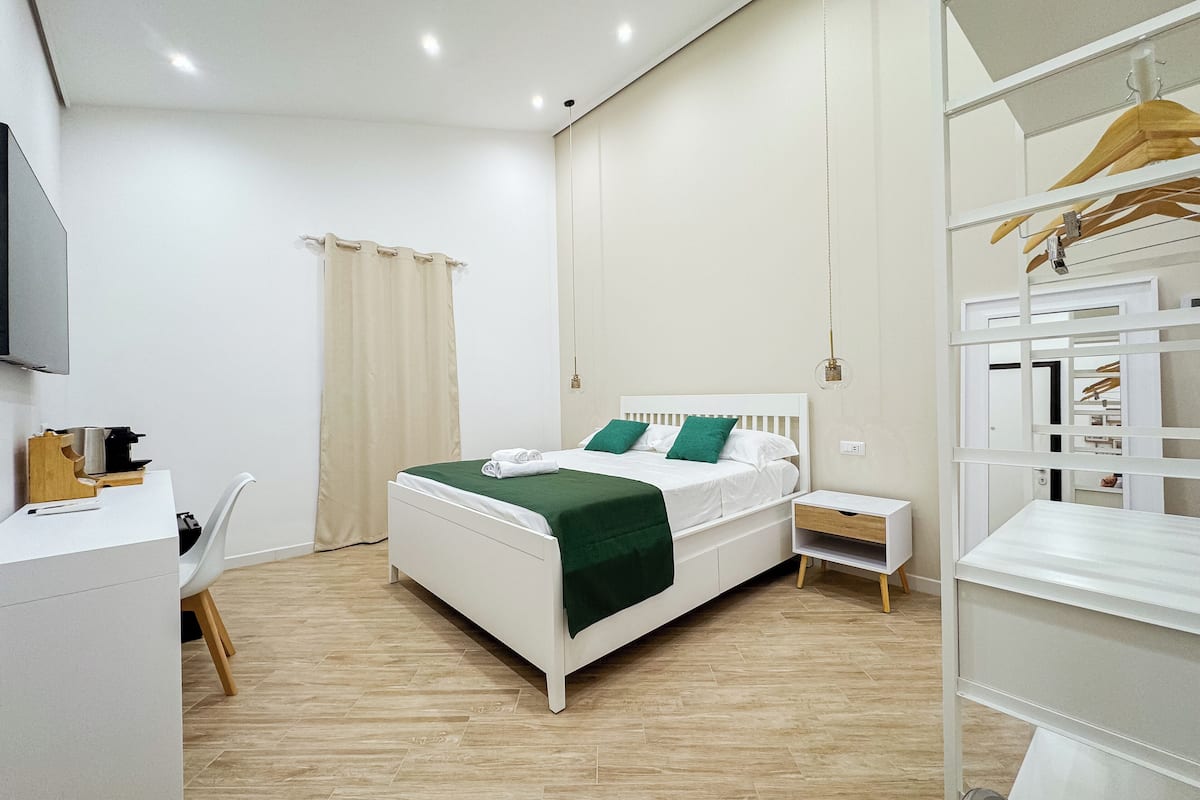 A modern hotel room with a bed, bedside tables, a desk, and a wardrobe.