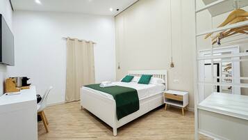A modern hotel room with a bed, bedside tables, a desk, and a wardrobe.