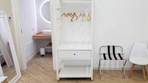 Habitación blanca con tocador, espejo, armario blanco con espacio para colgar ropa y una silla.