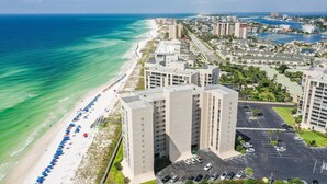 A beachfront hotel with multiple high-rise buildings, a beach with umbrellas, and a parking lot. - Shoreline Towers 3094 (Destin)