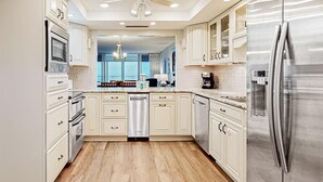 A modern kitchen with white cabinetry, stainless steel appliances, and a wooden floor. - Shoreline Towers 3094 (Destin)