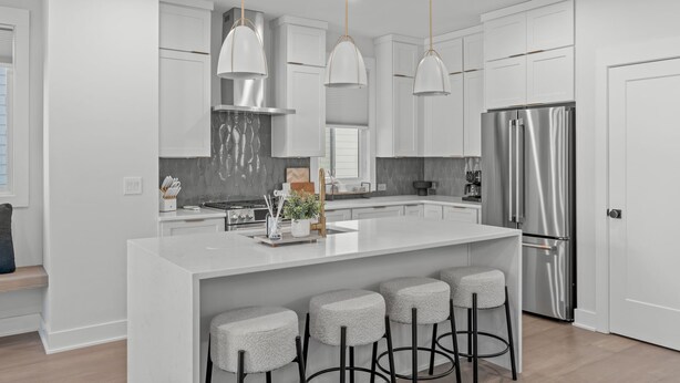 A modern kitchen with white cabinetry, stainless steel appliances, and a central island with bar stools. - Spacious 4 Bedroom House in Charming Downtown Raleigh with Amazing Views! (Raleigh)