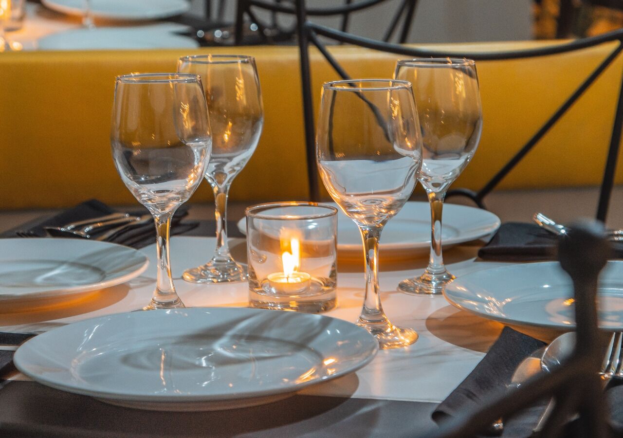 Une table à manger dressée avec de l’assiette blanche, des verres à vin transparents et une bougie allumée.