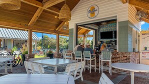 Ein Außenbereich mit einer Terrasse, Holztischen und -stühlen, einer Bar mit der Aufschrift "Peddlers Pub" und im Hintergrund Fahrräder.