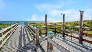 Ein hölzerner Steg führt zu einem Strand mit freiem Blick auf den Ozean.