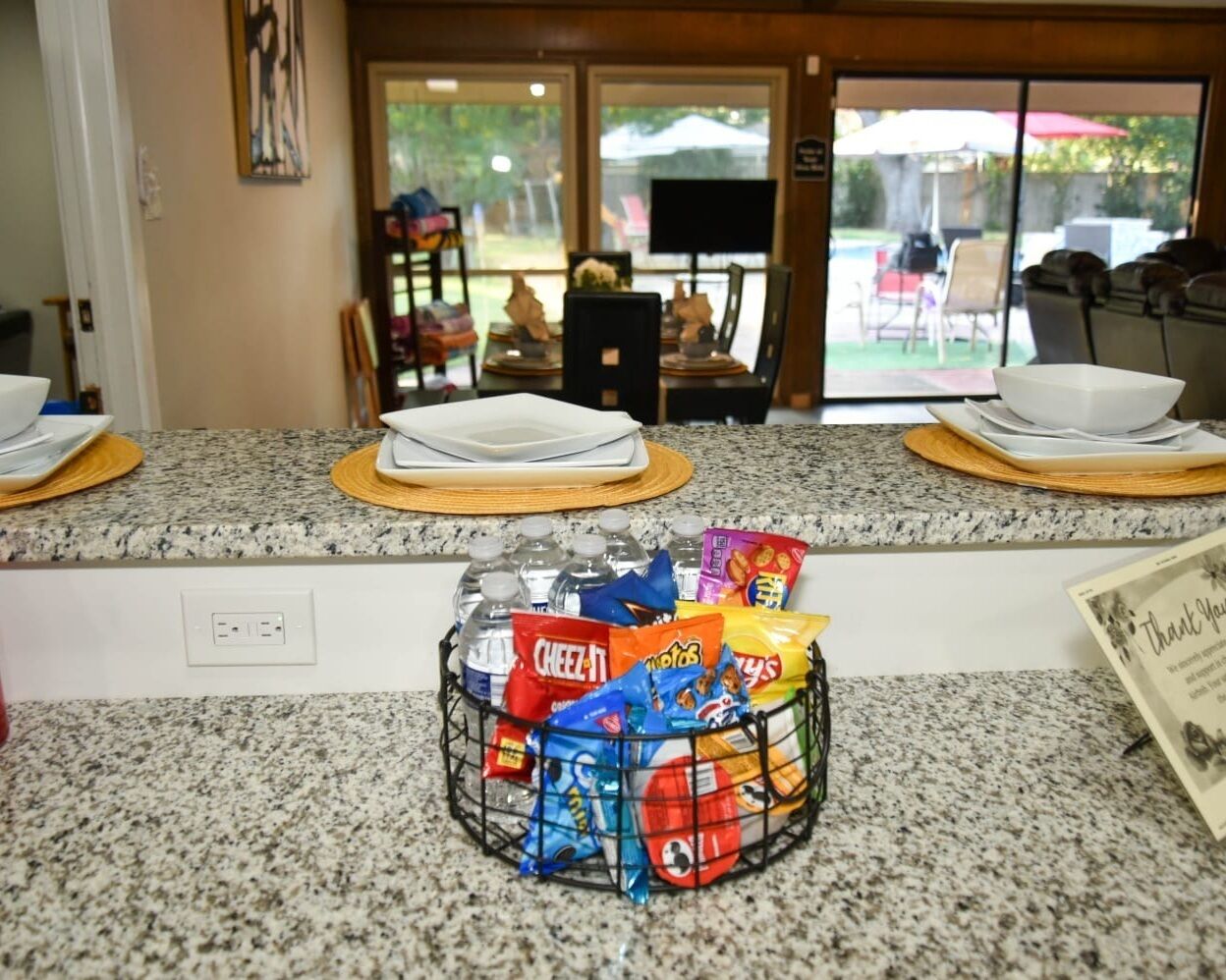 A kitchen counter with a snack basket containing various chips and a water bottle.