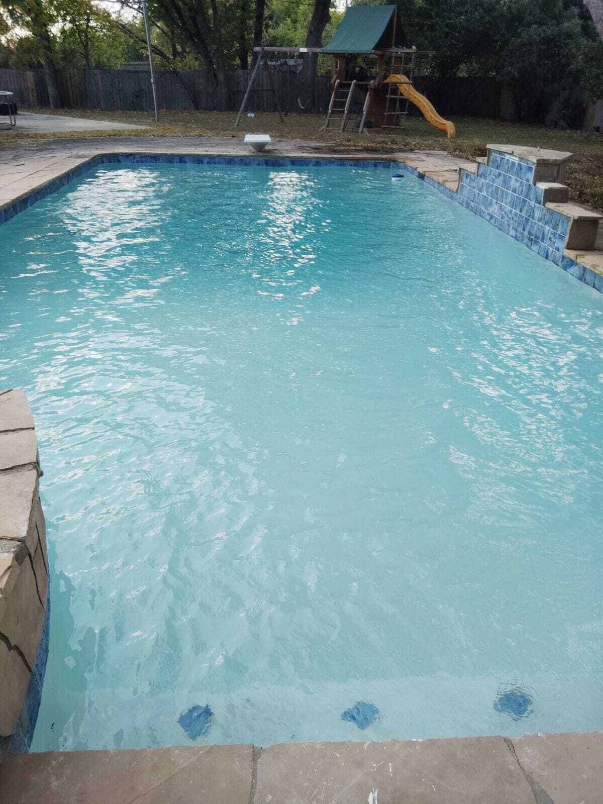 A rectangular swimming pool with a blue tiled edge and a stone border.