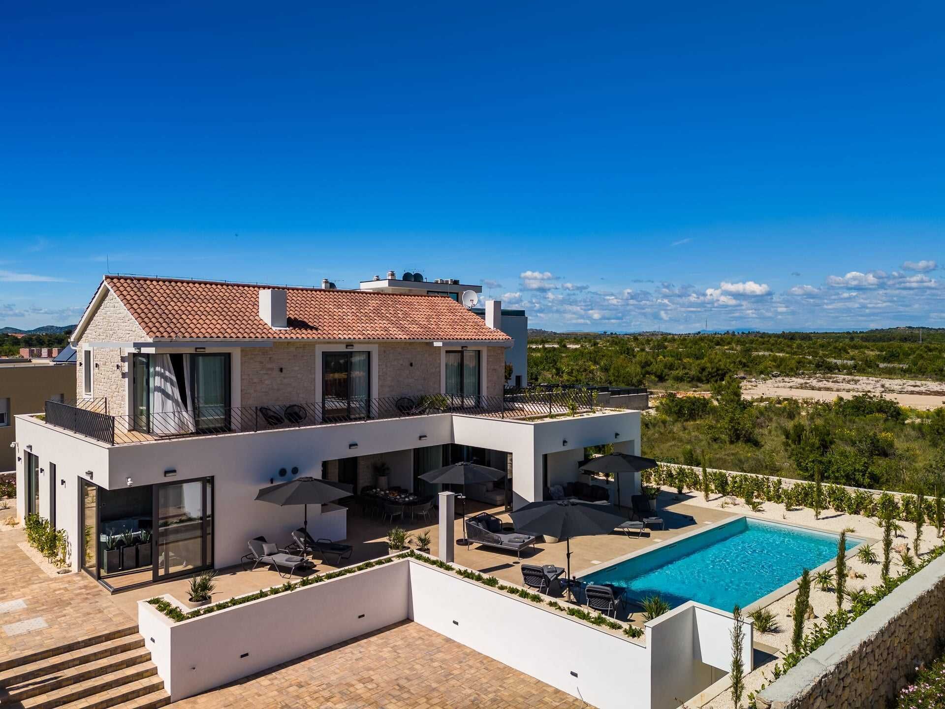 A modern two-story house with a swimming pool, outdoor seating, and a view of the surrounding landscape.