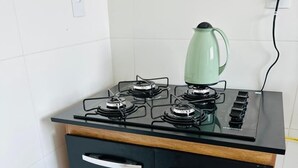 A compact kitchen with a gas stove, a kettle, and a black cabinet with two drawers. - CASA DAS FLORES (Praia Grande)