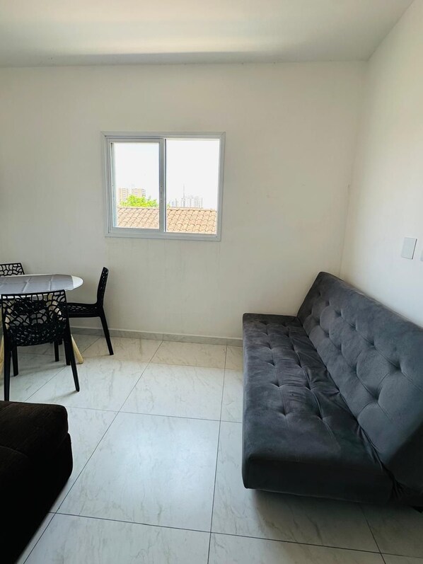 A room with a grey sofa, a dining table with chairs, and a window with a view of buildings.