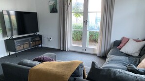 Un salon comprenant un canapé, un téléviseur et une porte-fenêtre coulissante donnant sur un jardin.