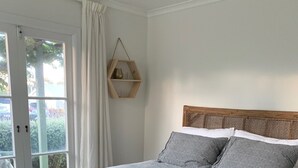 Une chambre à coucher avec un grand lit, une tête de lit en bois et une vue sur l’extérieur, visible à travers une porte vitrée.