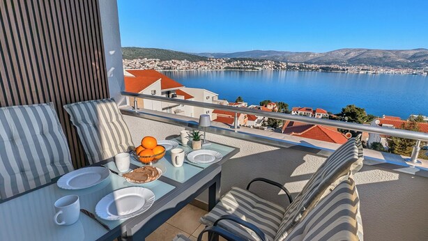 Un balcon avec une table dressée pour deux personnes, donnant sur une étendue d’eau et une ville côtière.