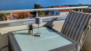 Un balcon avec une table en verre, une lampe et des coussins à rayures.