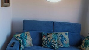 Un sofá azul con dos almohadones decorativos y un control remoto encima.