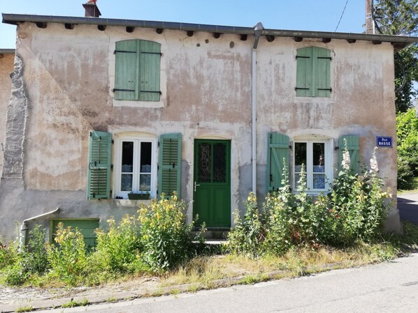 Un bâtiment à deux étages avec des volets verts, une porte bien visible et une enseigne indiquant « Rue BASSE ».