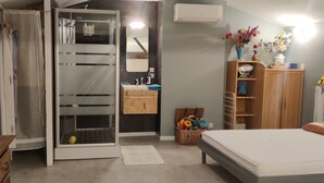 Ein Schlafzimmer mit Bett, einem Holzschrank, einem Badezimmer mit Waschbecken und Duschkabine.