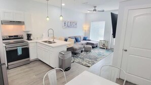 Cocina compacta con horno empotrado, pileta y cafetera. Hay una zona de estar con sofá y alfombra.