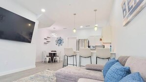 Una sala moderna con un televisor de pantalla plana, un sofá con cojines estampados y un comedor con sillas y una mesa.