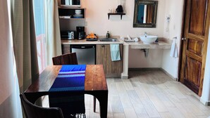 Une cuisine compacte équipée d’un four à micro-ondes, d’une machine à café et d’un évier. On y trouve une table à manger avec un chemin de table bleu et des chaises.