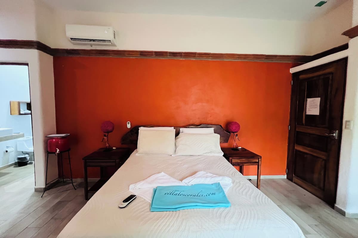 Une chambre d’hôtel avec un lit, une table de chevet, un appareil de climatisation et une porte en bois.