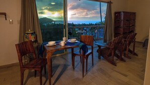 Un coin repas avec une table dressée pour quatre personnes, des chaises en bois et une vue sur l’océan grâce à de grandes portes-fenêtres coulissantes.