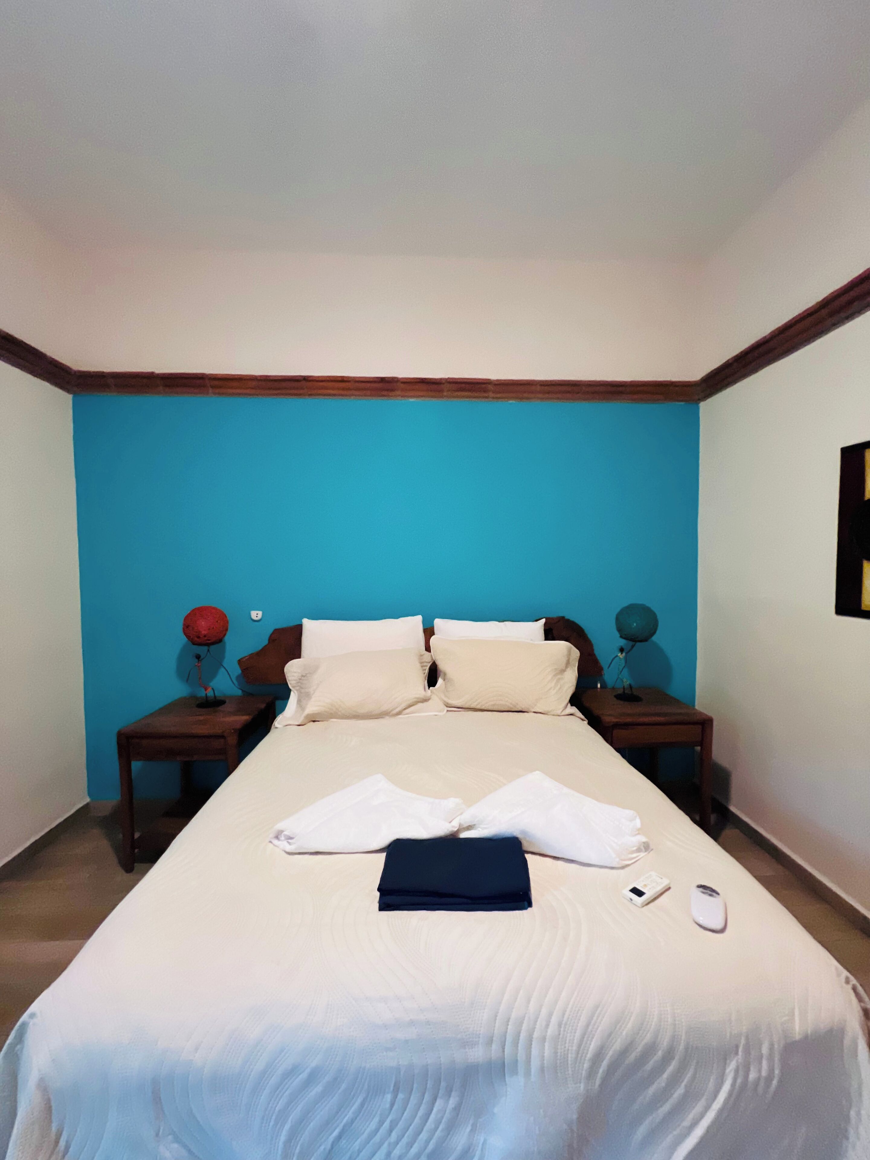 A neatly made bed with white linens, two bedside tables with lamps, and a blue accent wall.