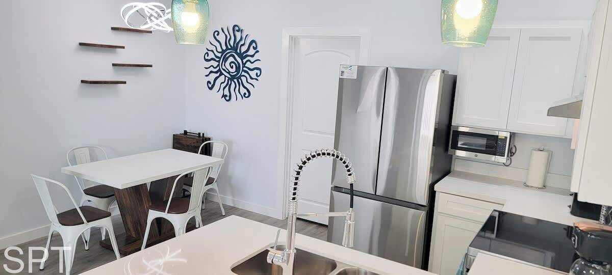 Une cuisine moderne dotée d’un réfrigérateur en acier inoxydable, de meubles blancs, d’un coin repas avec une table et des chaises blanches, et d’un élément décoratif mural.