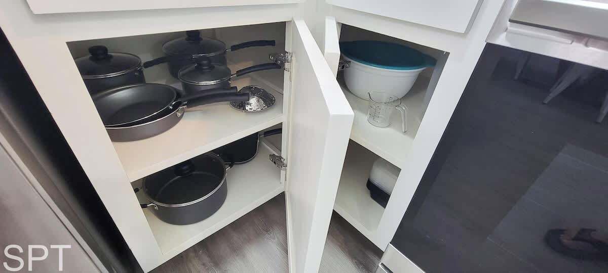 Une cuisine avec des armoires blanches, plusieurs poêles noires, un saladier blanc et un verre à mesurer.