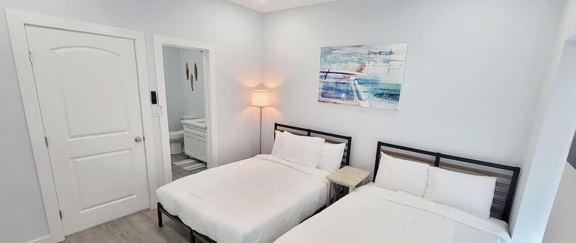 Habitación de hotel con dos camas, una mesita de noche, una lámpara y un cuadro en la pared.