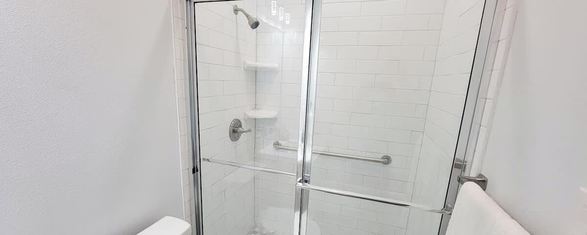 A glass-enclosed shower with a chrome faucet and a white tiled wall.