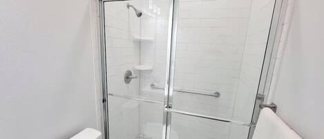 A glass-enclosed shower with a chrome faucet and a white tiled wall.