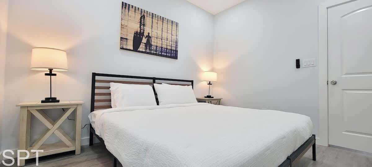 Un dormitorio con una cama grande, dos mesitas de noche con lámparas, un cuadro en la pared y una puerta.