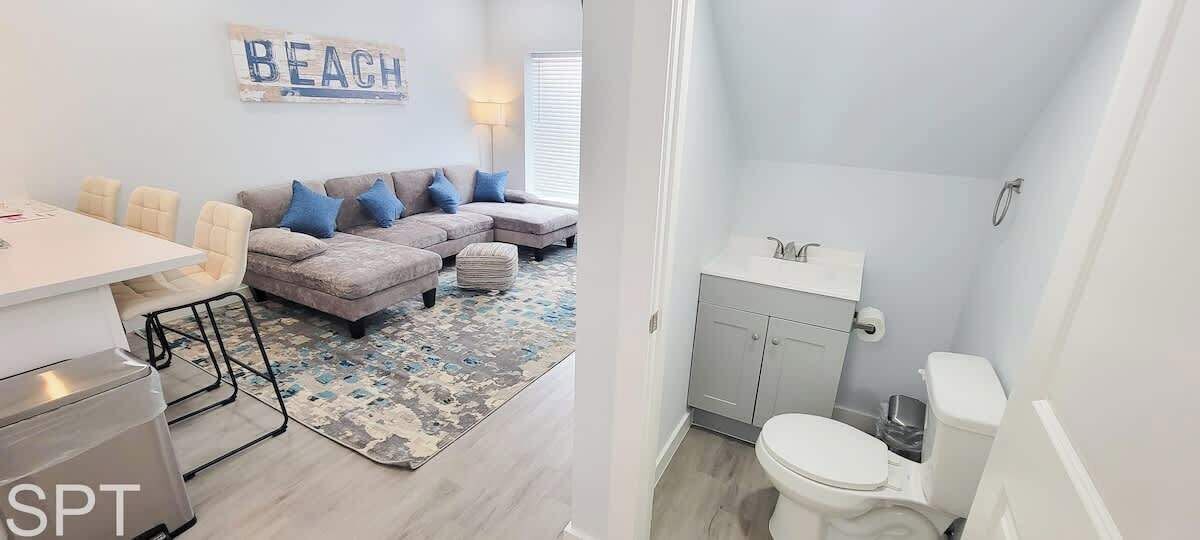 Un soggiorno moderno con divano, poltrone e tavolo da pranzo. Accanto, un bagno piccolo con toilette e lavandino.