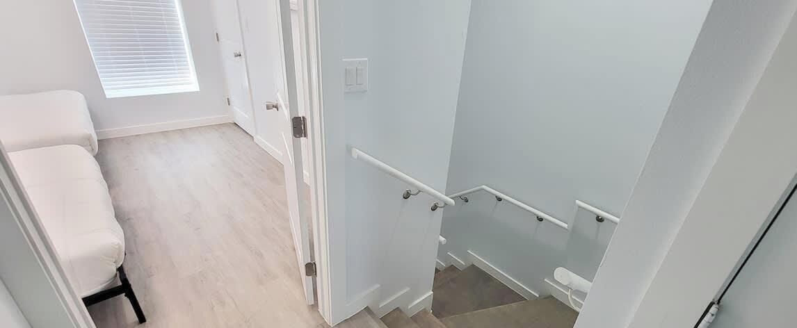 Un pasillo con un banco blanco, una puerta con manija blanca y una barandilla blanca.