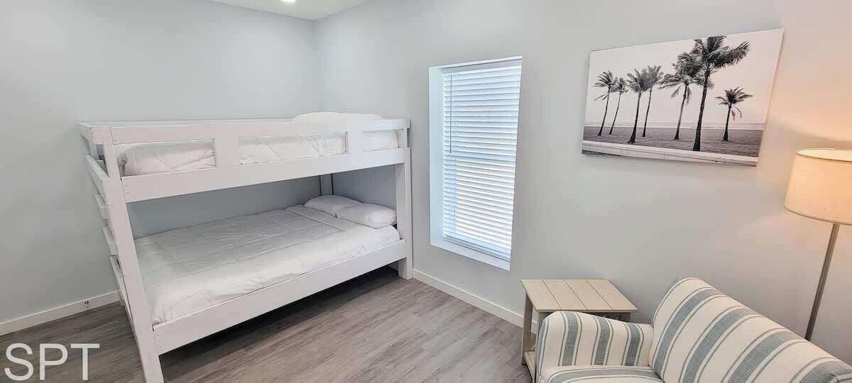 A bunk bed room with a window, a striped sofa, and a beach-themed painting on the wall.