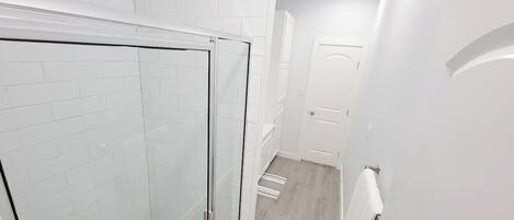 Baño con paredes de azulejos blancos, cabina de ducha de vidrio y suelo de madera.
