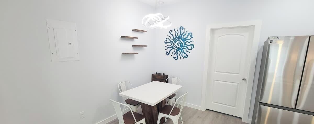 Una cocina con una mesa blanca, cuatro sillas, una puerta blanca y un refrigerador de acero inoxidable.