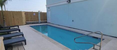 Una piscina con una escalera metálica, cerca de una valla de madera y una palmera.