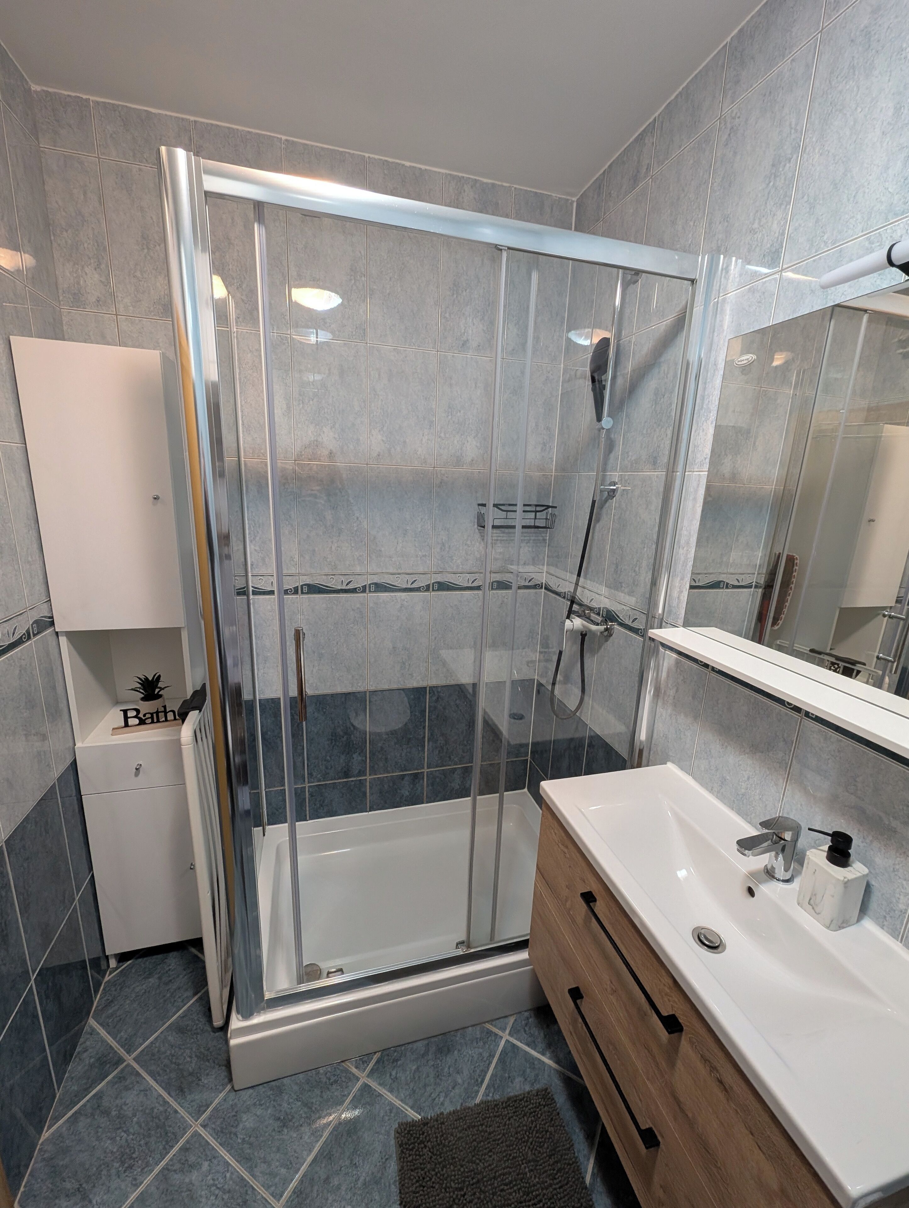 A modern bathroom with a glass-enclosed shower, a white sink, and a wooden vanity.