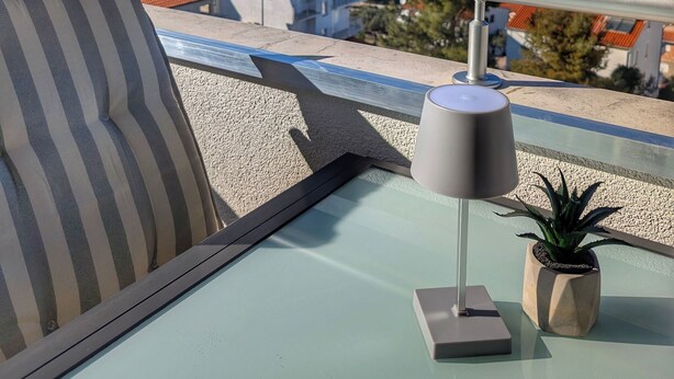 Ein Balkon mit Blick auf einen See und Berge, ein gestreifter Kissen, eine Lampe und ein Topfpflanze.