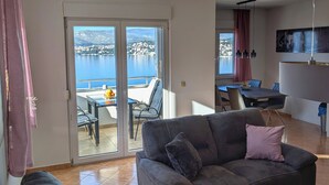 Ein Wohnzimmer mit einer Couch, einem Holztisch und Blick auf einen Balkon mit Tisch und Stühlen.