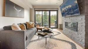A modern living room with a grey sofa, a coffee table, a fireplace, and a large window with a mountain view.