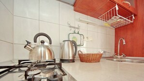 Une cuisine équipée d’une cuisinière à gaz, d’une bouilloire et d’un panier posé sur le plan de travail.