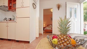 Une cuisine avec des meubles blancs et une table en osier sur laquelle se trouve un panier de fruits.
