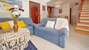 A living room with a blue sofa, yellow pillows, a white table with a lace tablecloth, and a vase with flowers. - Seafront Apartments Deveron - Duplex Two Bedroom Apartment with Balcony and Sea View (Jelsa)