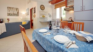 A dining area with a blue tablecloth, white plates, and cutlery. There is a kitchen in the background with wooden cabinets and a stove. - Seafront Apartments Deveron - Duplex Two Bedroom Apartment with Balcony and Sea View (Jelsa)